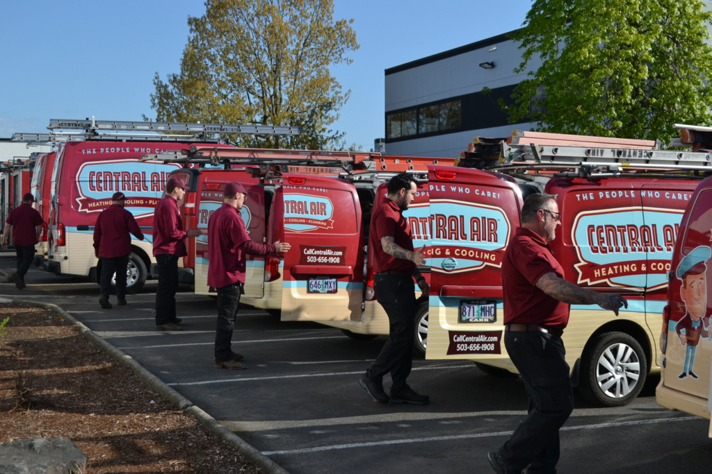 Photo of several Central Air HVAC technicians opening the backs of a fleet of branded vans